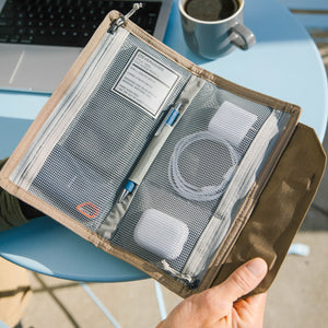 Hand holding a CIVIC Access Pouch 1L in Fossil Brown travel organizer with mesh pockets on a blue chair.