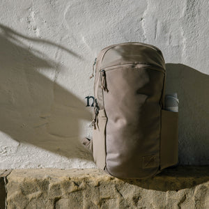 CIVIC Half Zip 22L in Fossil Brown backpack leaning against a textured wall