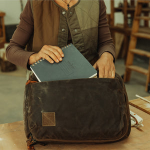CIVIC Panel Loader 16L in waxed tan - packing the side access pocket with a notebook.