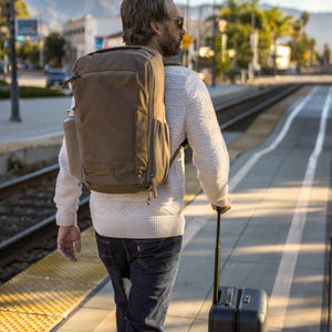 Man with a CIVIC Travel Bag 26L in Fossil Brown backpack and suitcase walking on a train platform