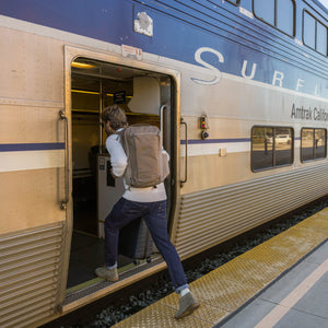 Person boarding an Amtrak train on a platform wearing a CIVIC Travel Bag 26L in Fossil Brown