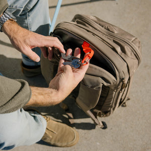 Person organizing tools on a key leash of a CIVIC Travel Bag 26L in Fossil Brown backpack on a concrete surface