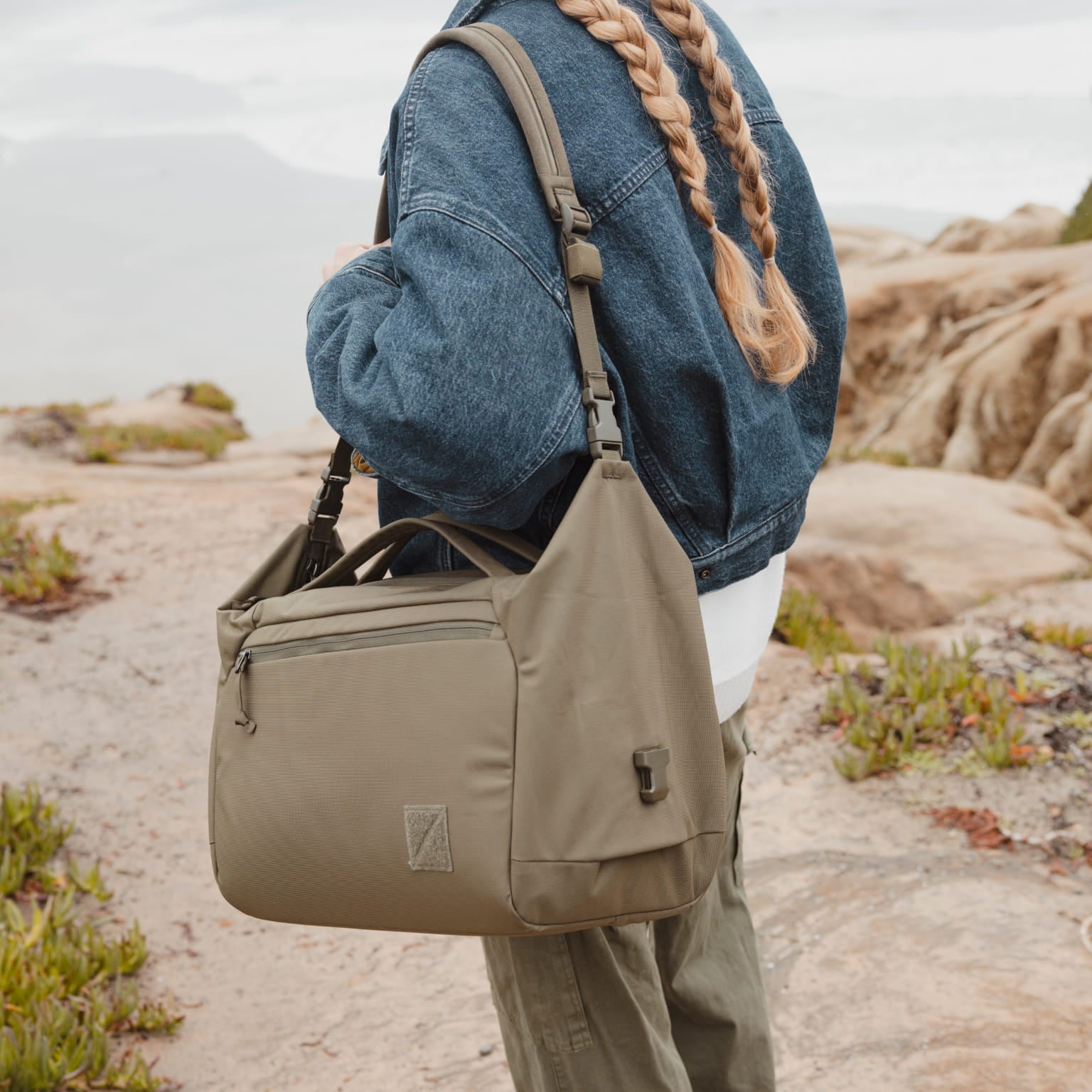 Person wearing a denim jacket and carrying a OD Green Transit Duffel in a desert setting