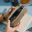 Person opening a CIVIC Access Pouch 0.5L in Fossil Brown travel organizer with items inside, sitting on a blue surface. Person opening a CIVIC Access Pouch 0.5L in Fossil Brown travel organizer with items inside, sitting on a blue surface. [13017a-FBN