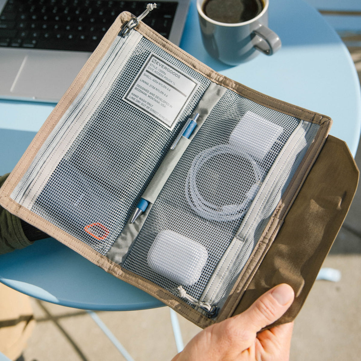 Hand holding a CIVIC Access Pouch 1L in Fossil Brown  travel organizer with mesh pockets on a blue chair.