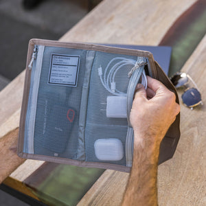 Person holding a CIVIC Access Pouch 1L in Fossil Brown - travel organizer with mesh pockets on a wooden surface
