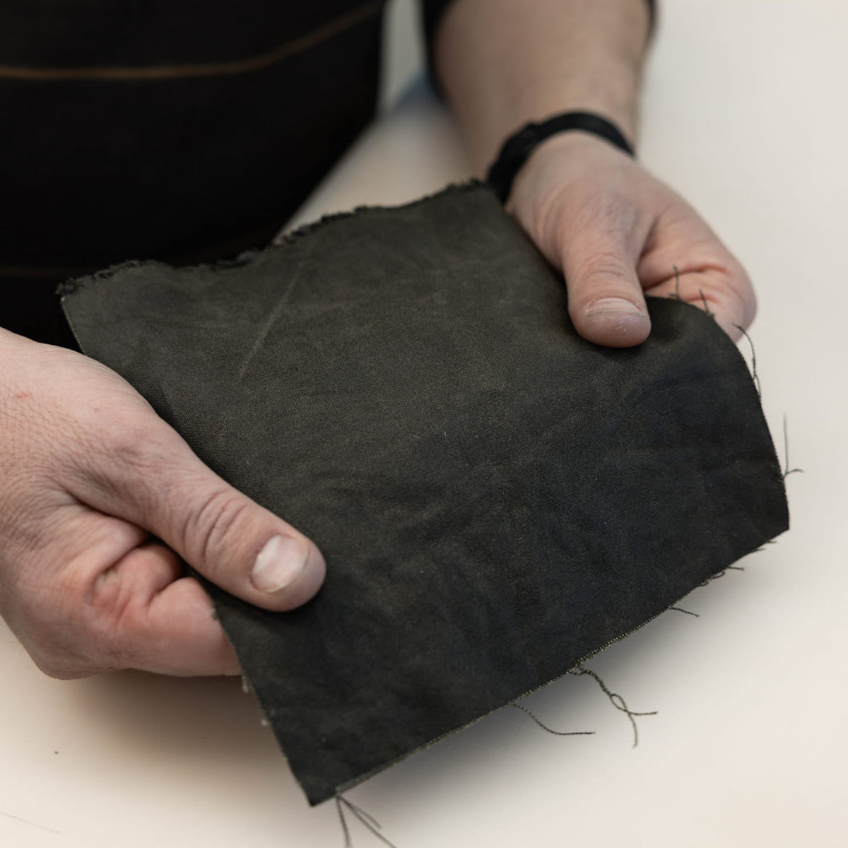 Person holding a piece of waxed canvas fabric on a light background [13019cc-WOL, 13012cc-WOL]