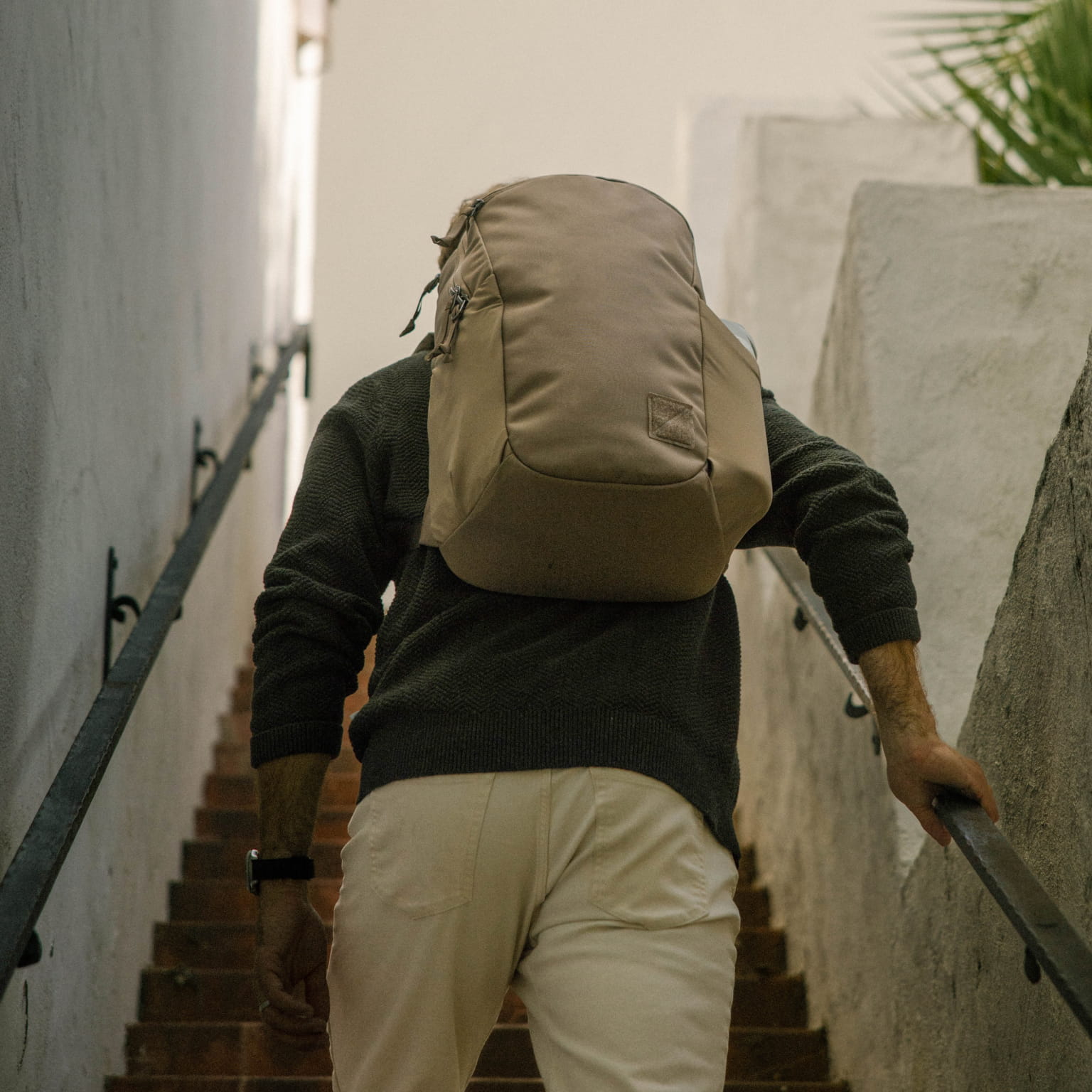 Person with a CIVIC Half Zip 22L in Fossil Brown backpack climbing stairs in an urban setting [13003d-FBN]