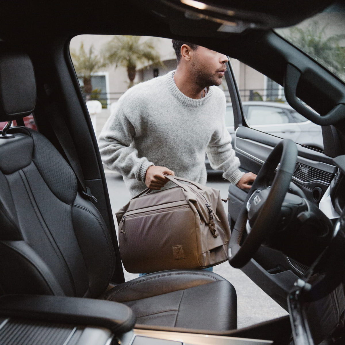 Man getting into a car with a Transit Duffel 25L in Fossil Brown , viewed from inside the vehicle.