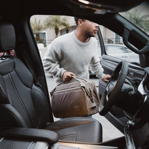 Man getting into a car with a Transit Duffel 25L in Fossil Brown , viewed from inside the vehicle.