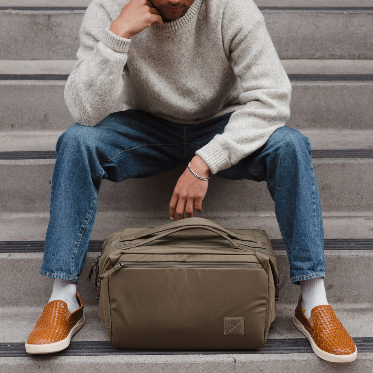 Person sitting on steps with a Transit Duffel 25L in OD Green in front of them