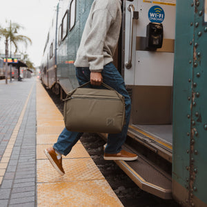 Person boarding a train with a Transit Duffel 25L in OD Green at a station platform visible